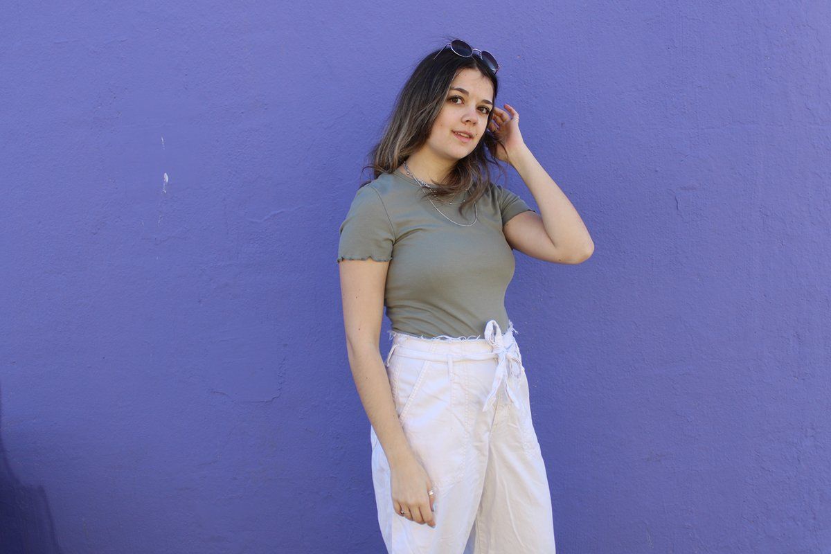 A woman in a green shirt and white pants is standing in front of a purple wall.