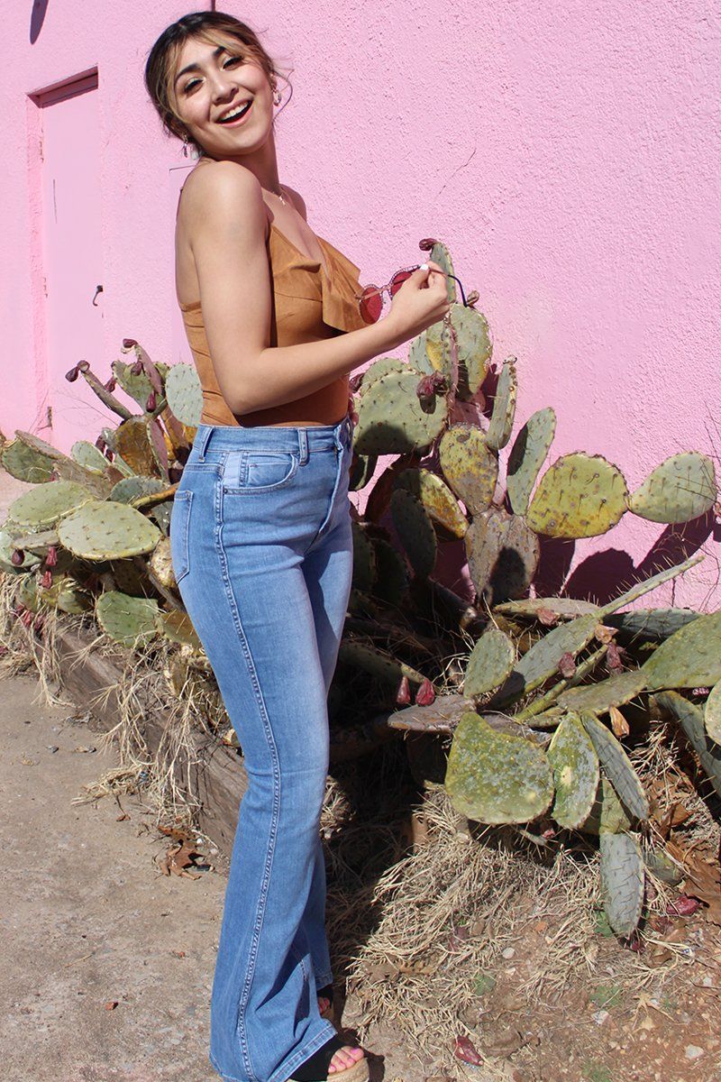 A woman is standing next to a cactus in front of a pink wall.