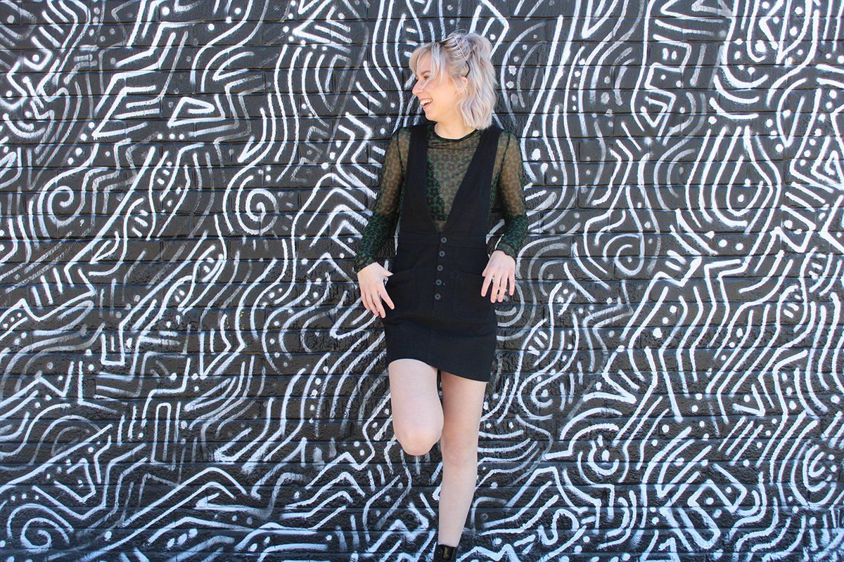A woman in a black dress is standing in front of a black and white wall.