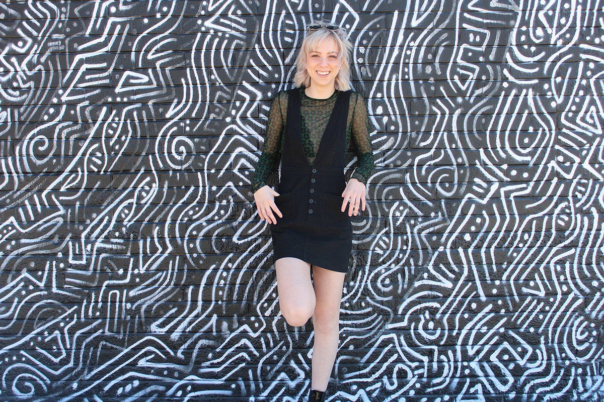 A woman in a black dress is standing in front of a black and white wall.