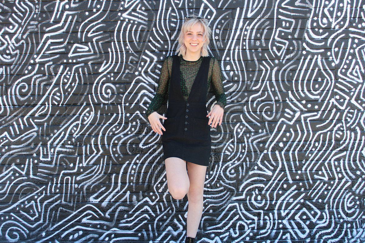 A woman in a black dress is standing in front of a black and white wall.