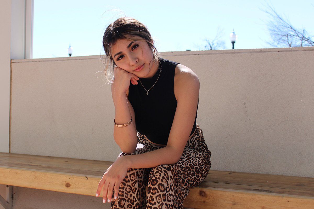 A woman is sitting on a wooden bench with her hand on her chin.