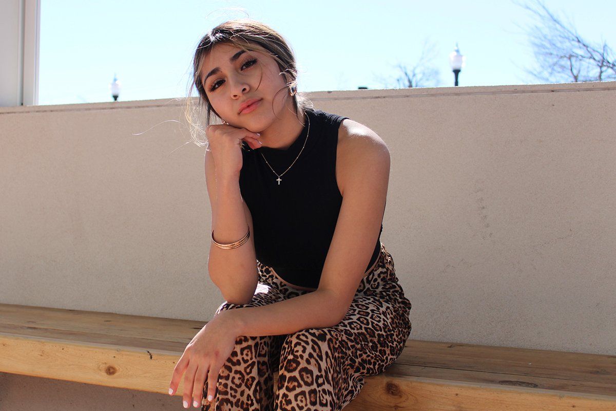 A woman is sitting on a wooden bench with her hand on her chin.