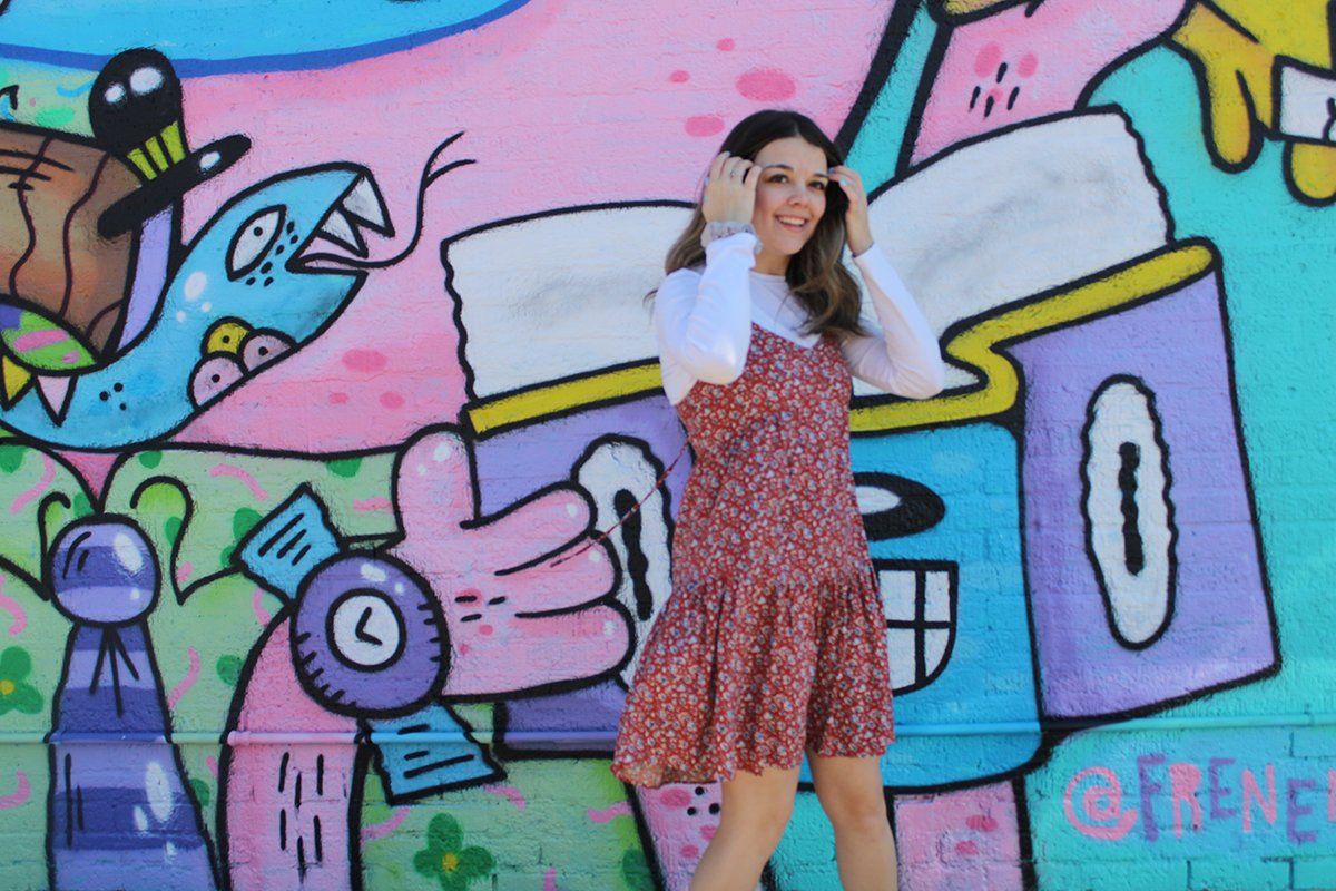 A woman in a red dress is standing in front of a colorful graffiti wall.