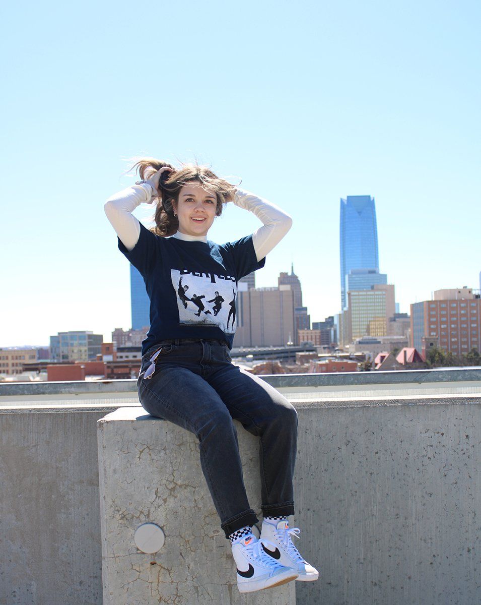 A woman is sitting on a wall with her hands in her hair.