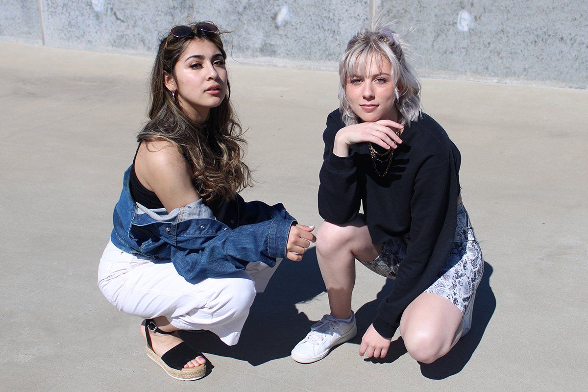 Two women are squatting down on the ground holding hands.