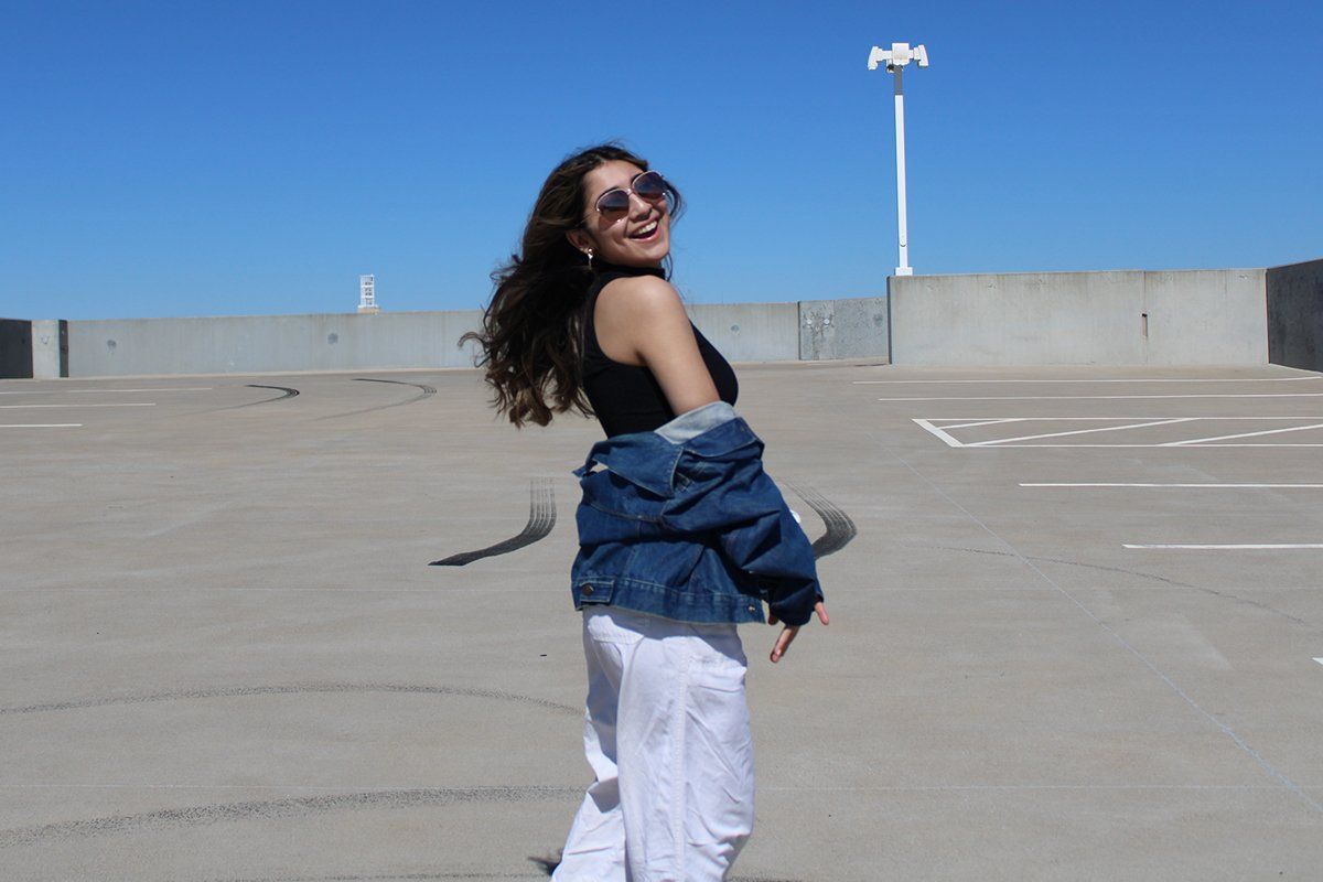 A woman wearing sunglasses and a denim jacket is standing in a parking lot.