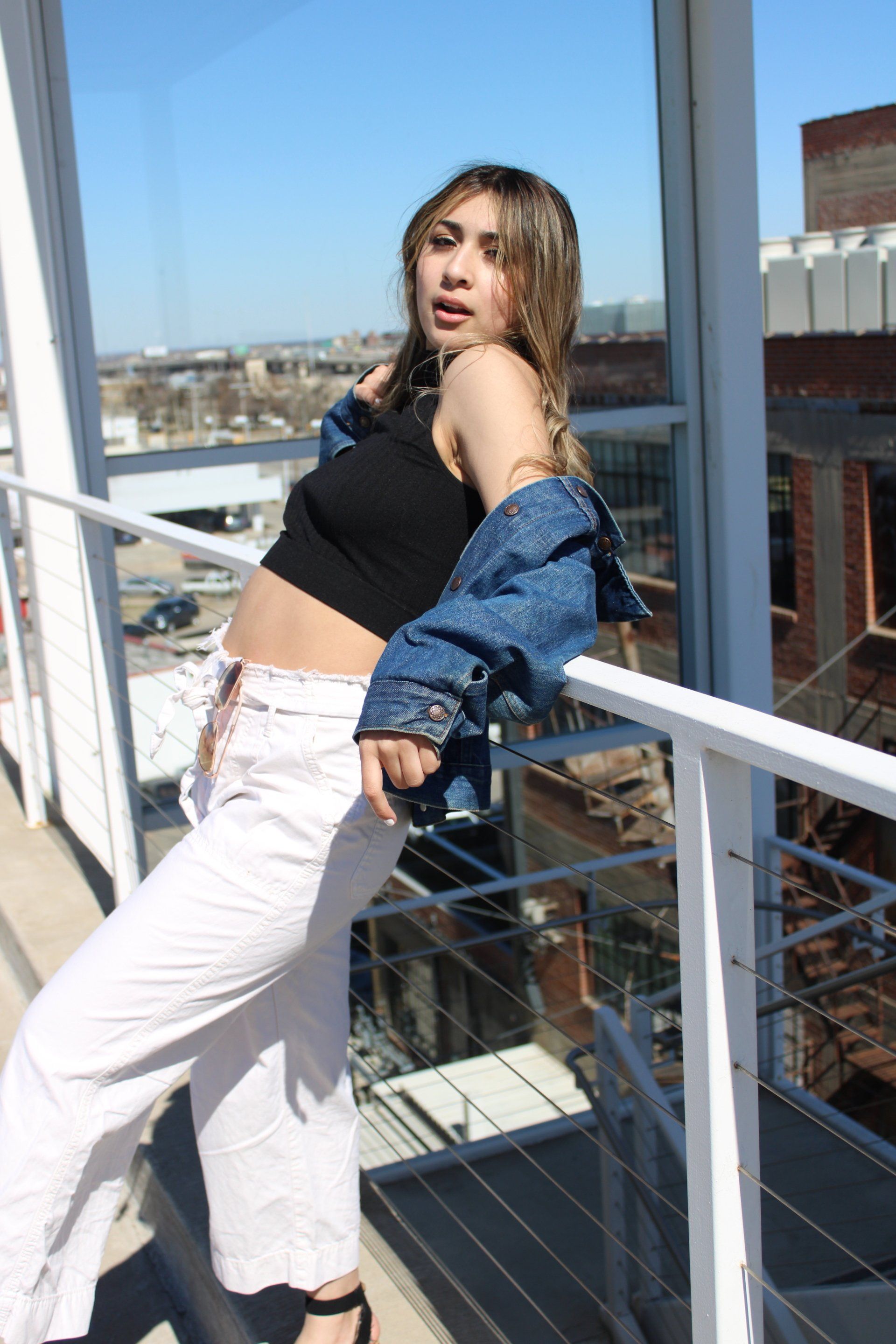 A woman in a black crop top and white pants is standing on a balcony.