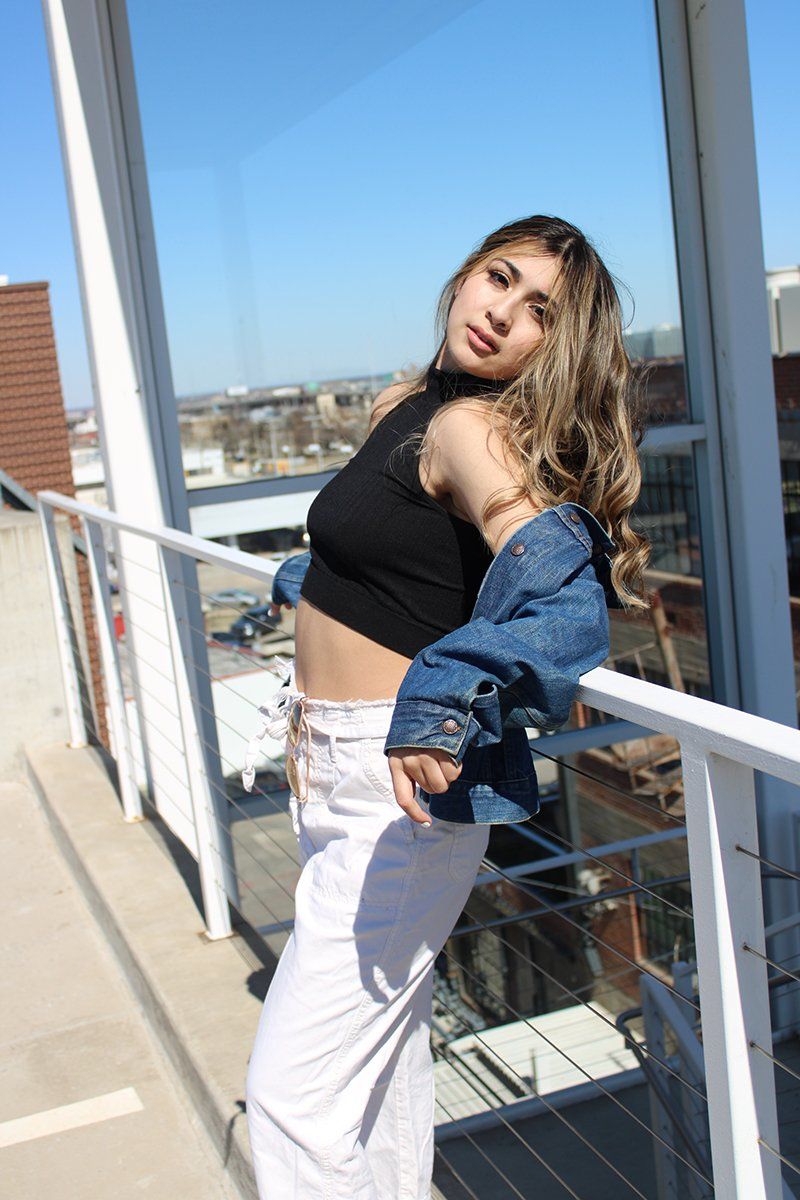 A woman in a black crop top and white pants is standing on a balcony.