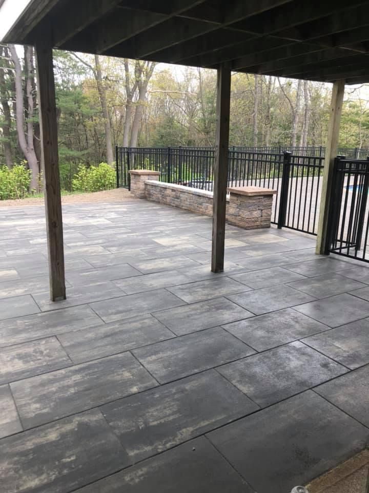Covered stone patio with black posts, railing, and a stone bench overlooking trees