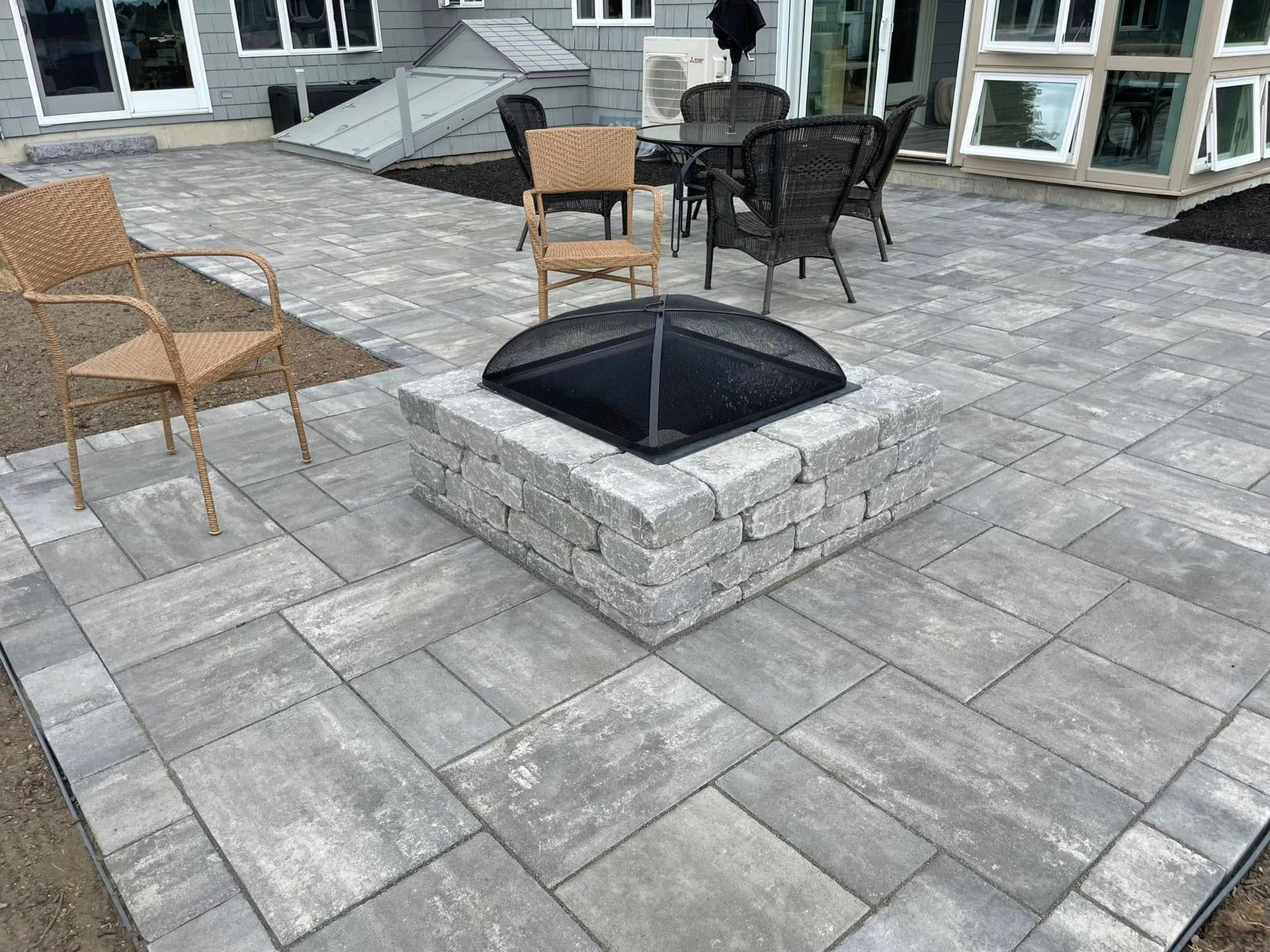 Patio with gray pavers, outdoor chairs, and a central umbrella base in front of a building