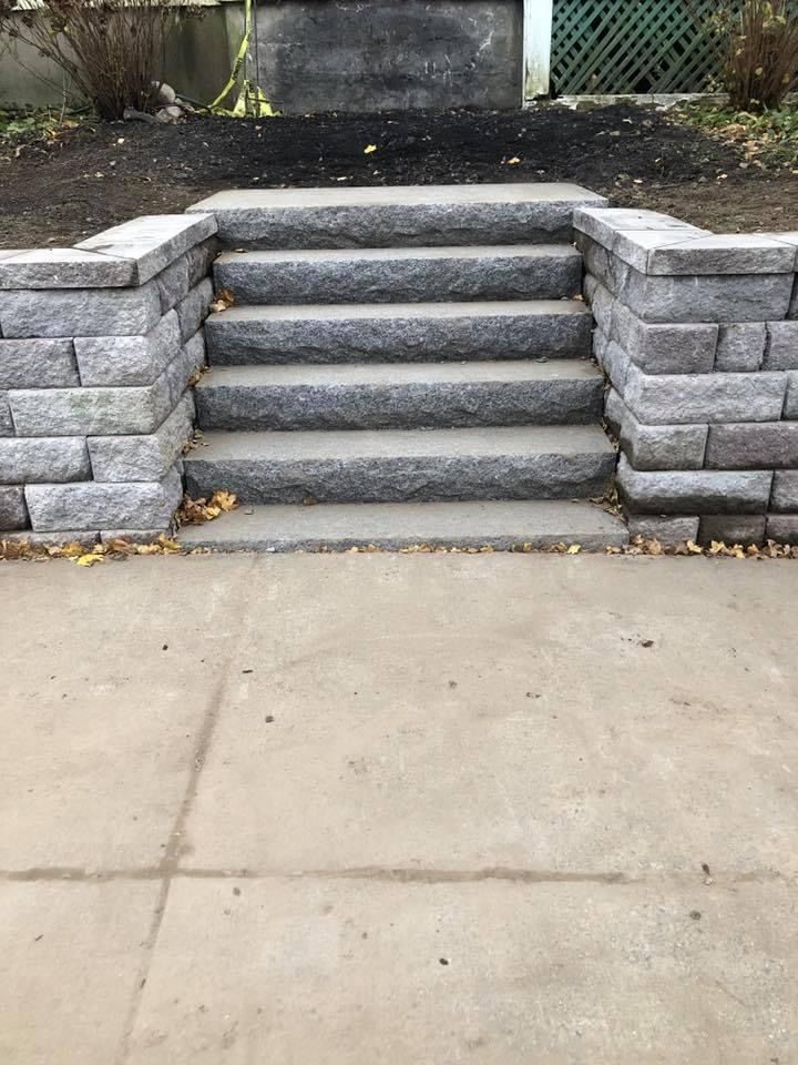 Stone steps leading up from a sidewalk, flanked by gray retaining walls.