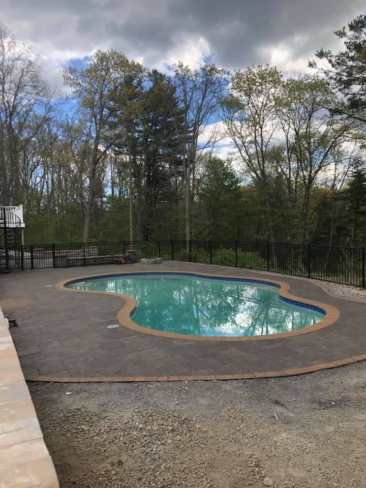 Outdoor backyard pool with turquoise water, surrounded by a wooden deck and trees under a cloudy sky