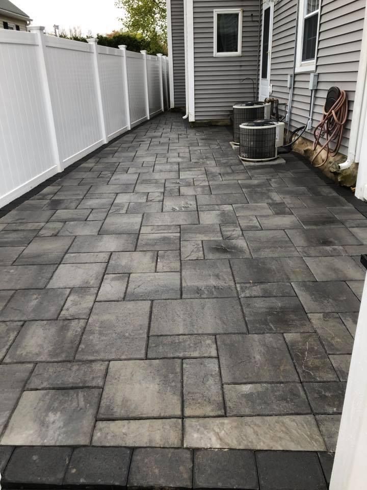 Narrow backyard walkway with gray paver stones beside a house and white fence
