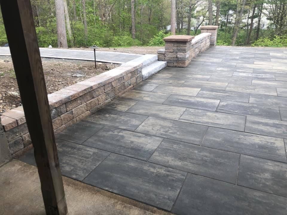 Stone patio with low retaining wall and stairs overlooking a wooded yard
