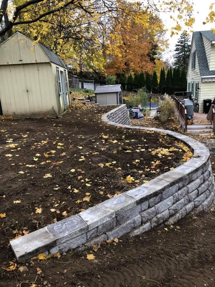 Curved stone retaining wall edging a freshly landscaped yard beside houses in autumn.