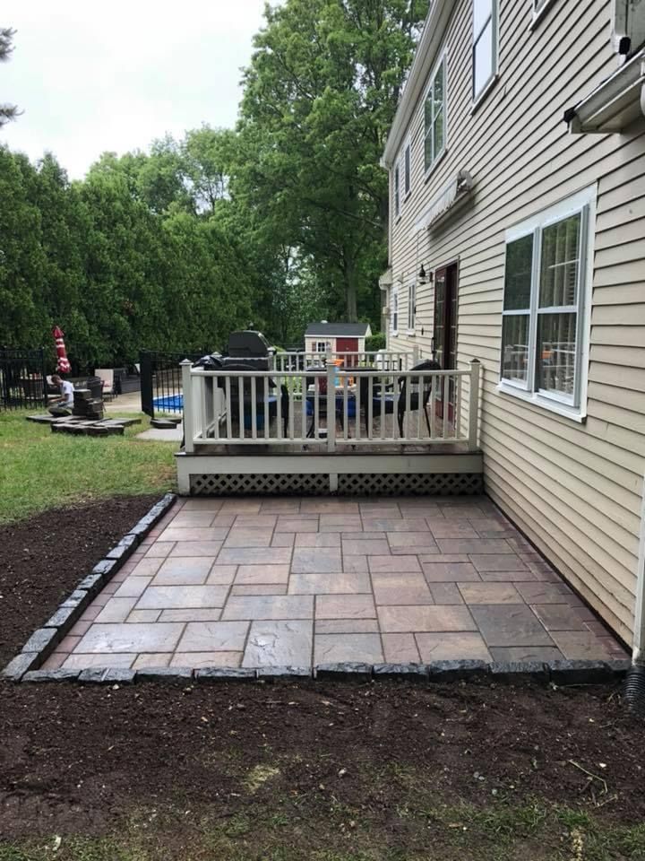 Backyard patio with stone pavers and a small wooden deck beside a beige house