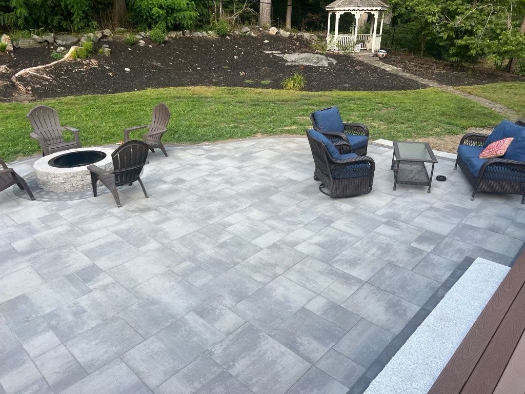 Patio with gray pavers, black fire pit and chairs, blue cushioned seating, and a garden backdrop