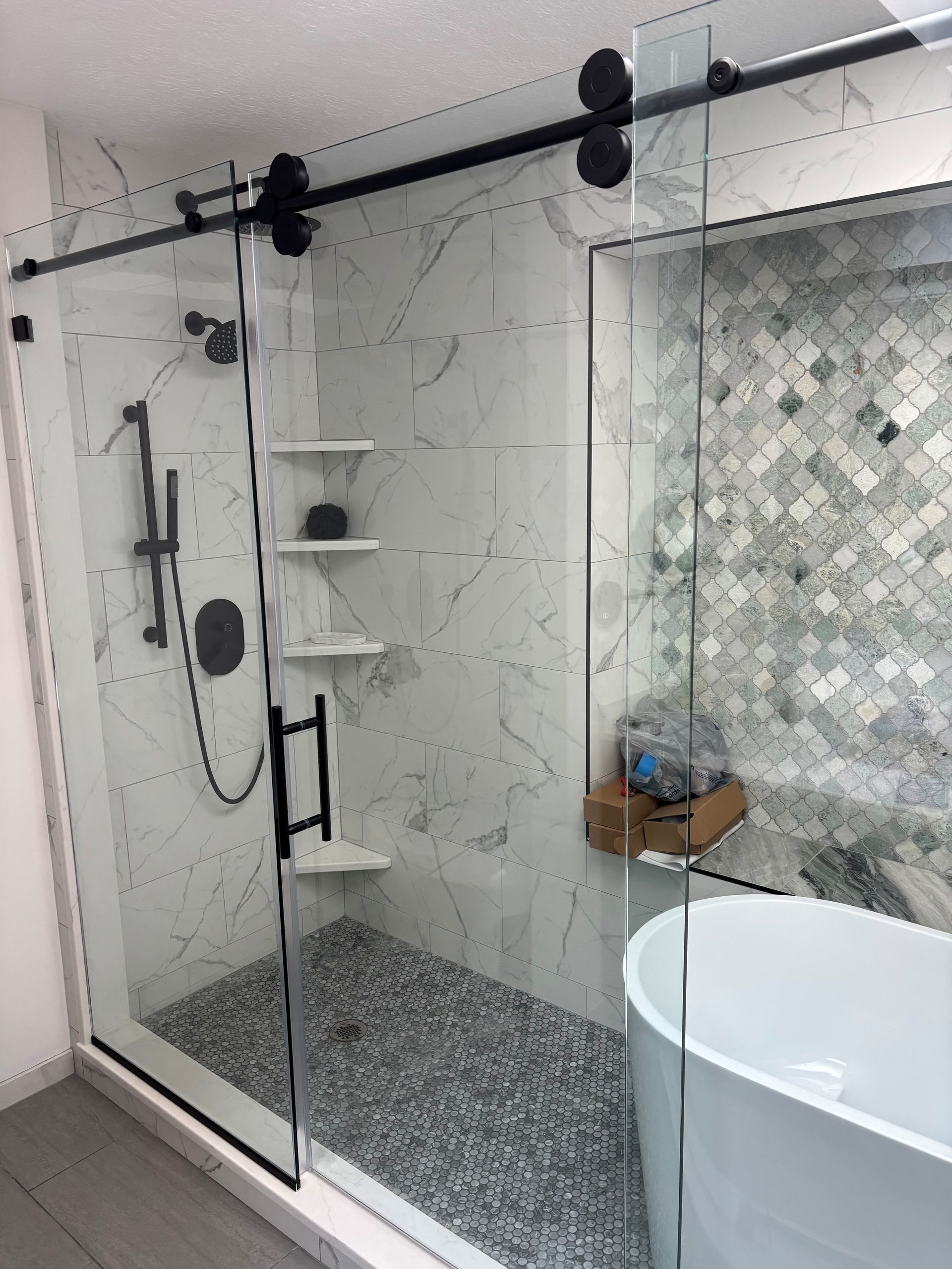 Modern bathroom with a glass shower, black fixtures, and marble tile.