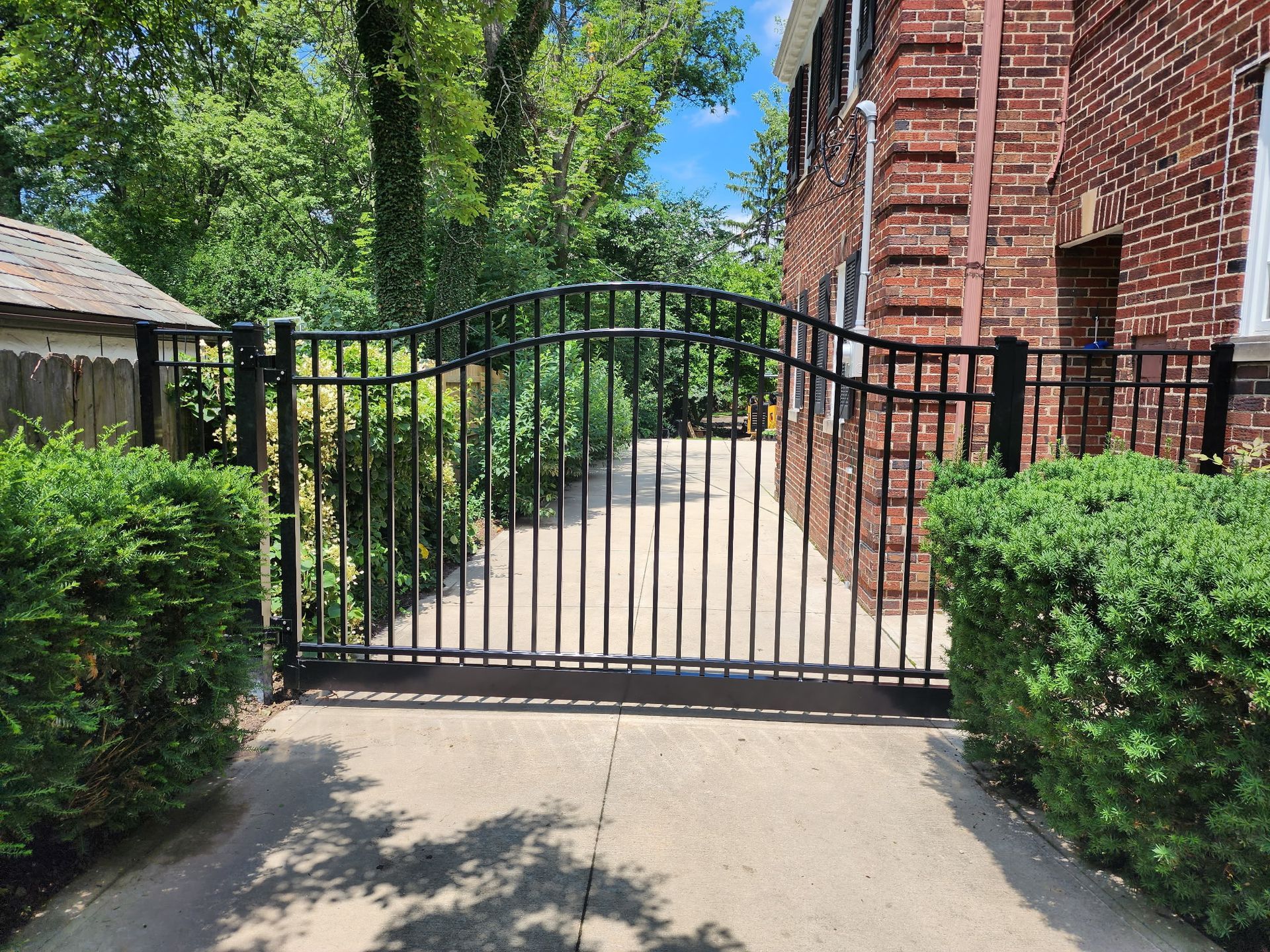 A black fence is surrounding a driveway leading to a brick building.