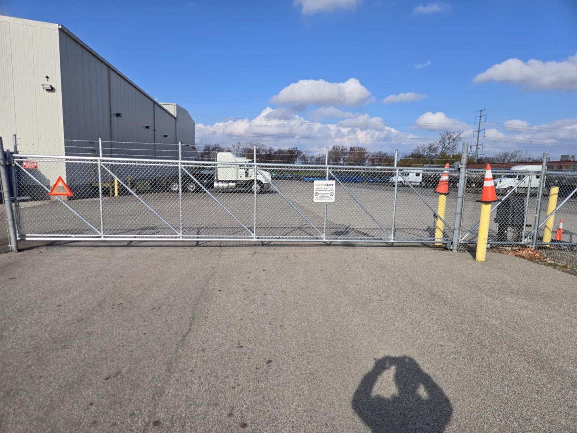 A shadow of a person is cast on the ground in front of a fence