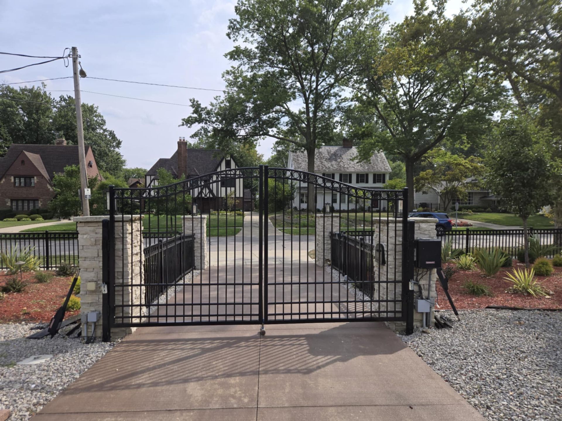 A black gate is open to a driveway in front of a house.
