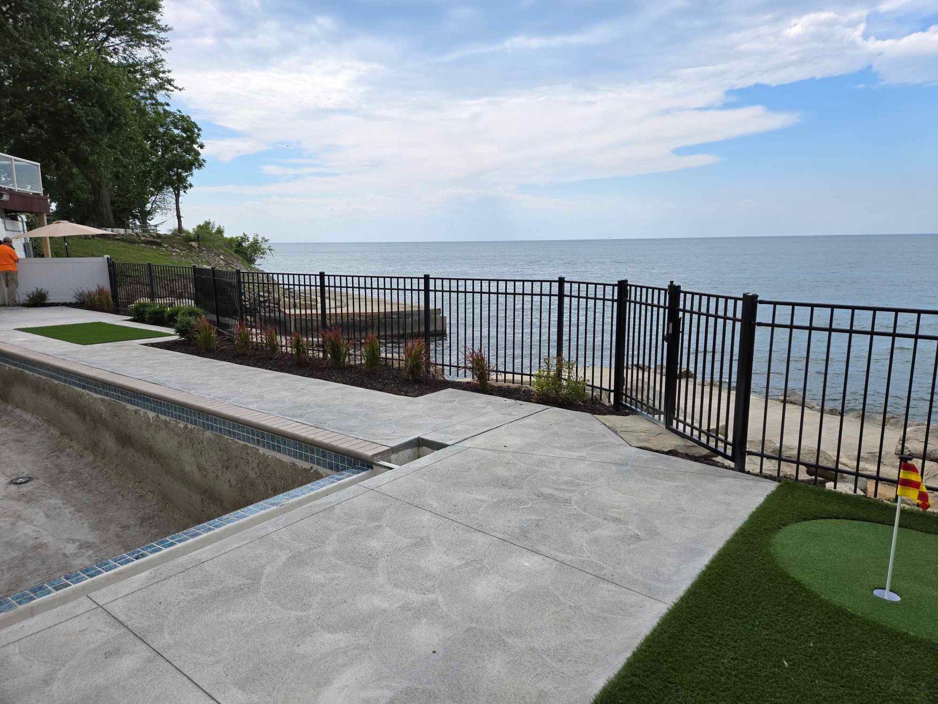 There is a putting green next to a pool with a view of the ocean.