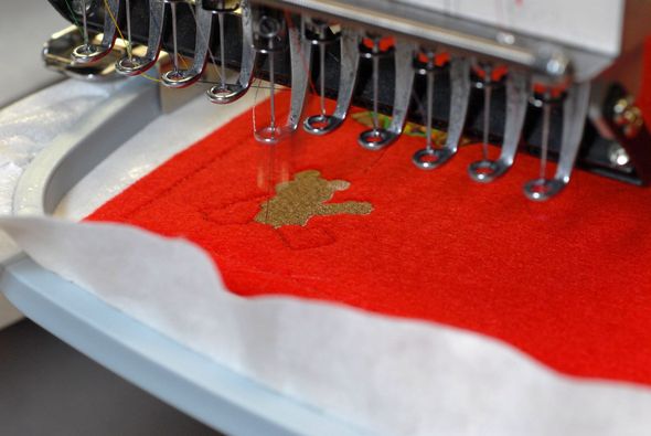 Embroidery machine stitching gold design onto red fabric, close-up shot.