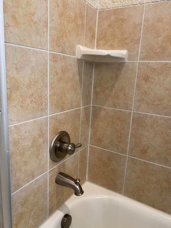 Beige tiled shower with faucet, tub spout, and soap dish.