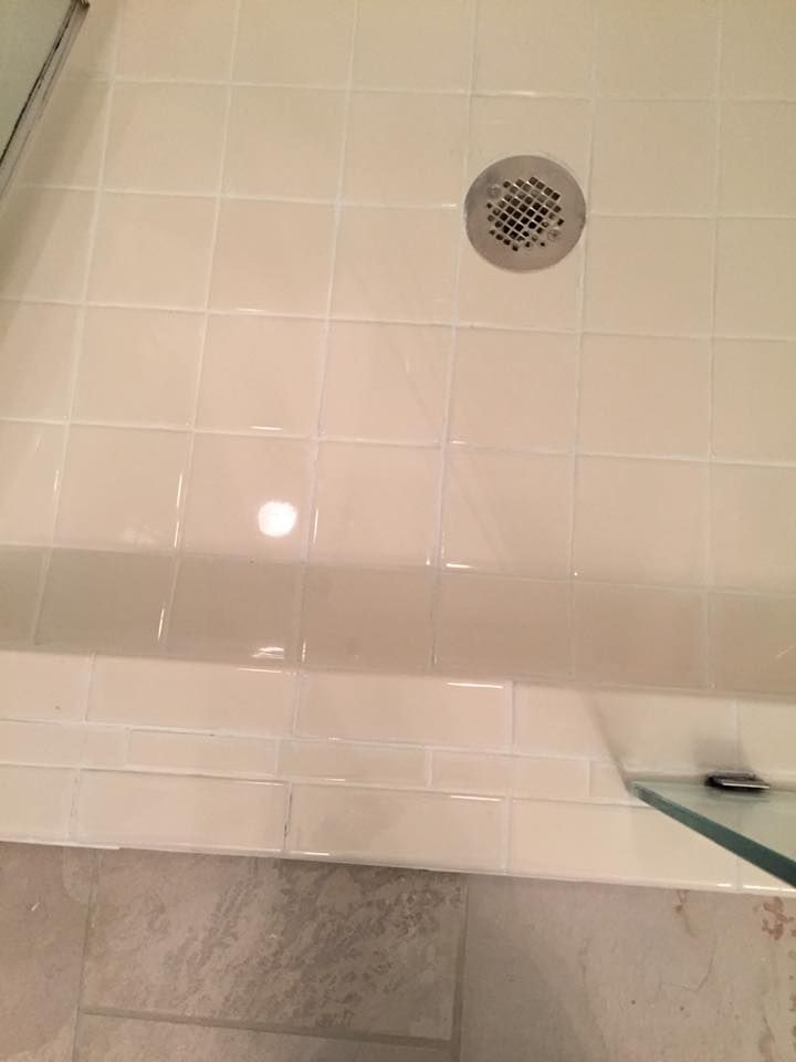 White tiled shower floor with drain, shelf, and glass shower door.
