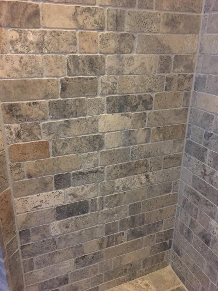 Stone tile wall in a bathroom, with various shades of gray, beige, and brown.