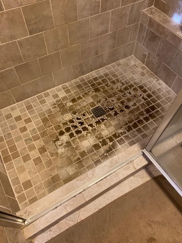 Shower floor with brown tiles and dark stains around the drain.