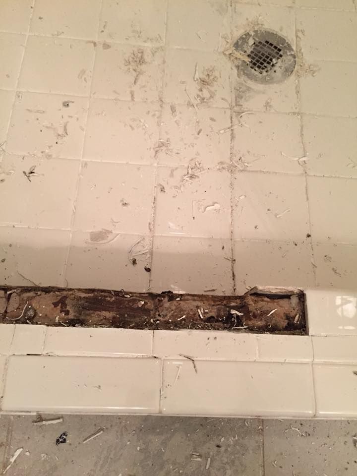 Damaged tile shower floor, showing exposed wood, debris, and drain.