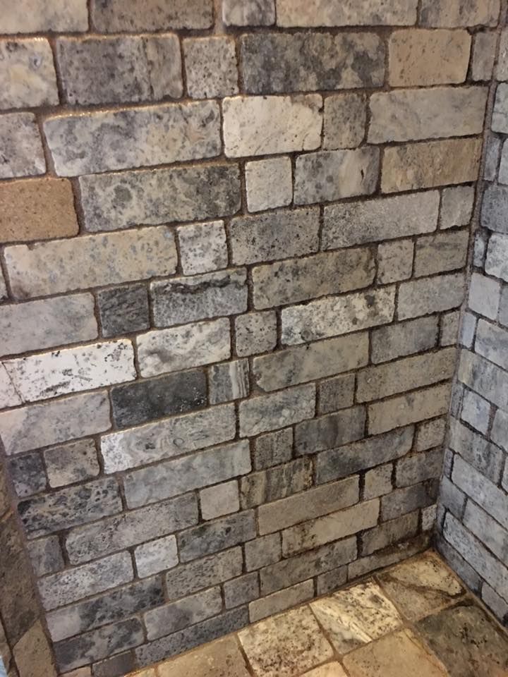 Brick wall corner with gray, beige, and white bricks. Dark grout. The floor is tiled.
