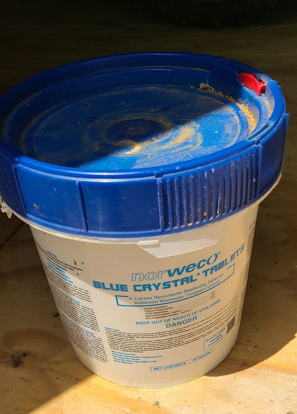 White bucket with blue lid and yellow powder on top, in sunlight.
