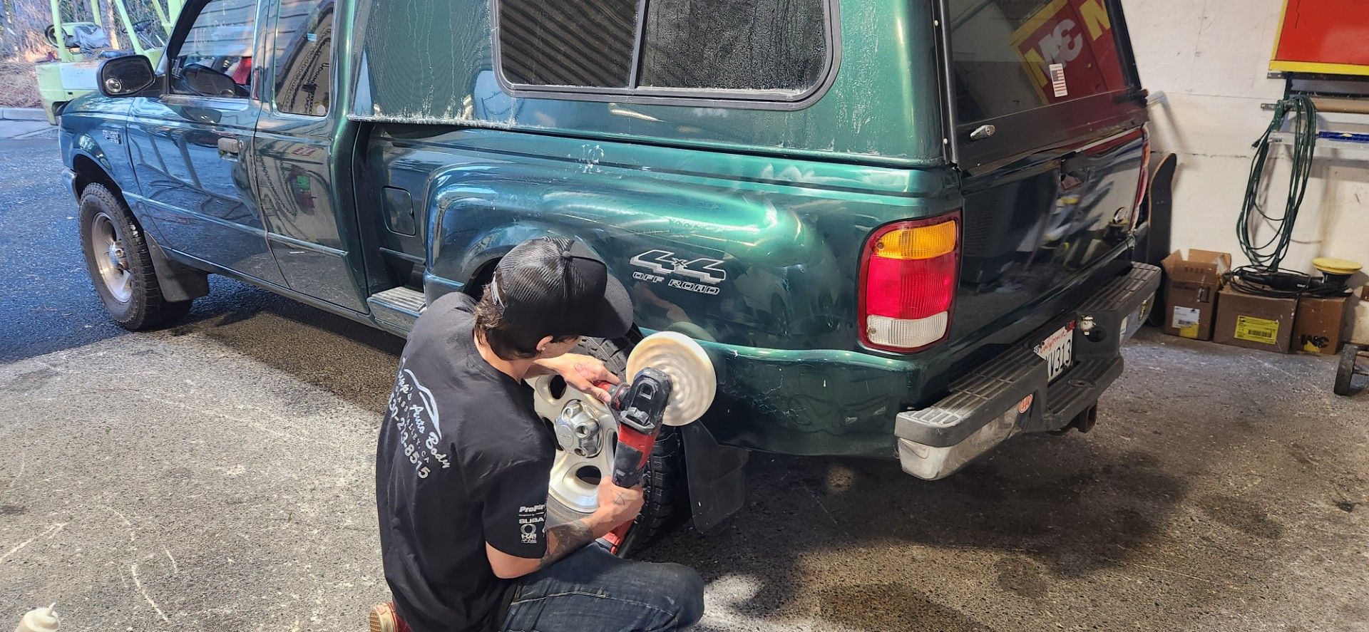 Person polishing the side of a green pickup truck with a machine. The truck has a camper shell.