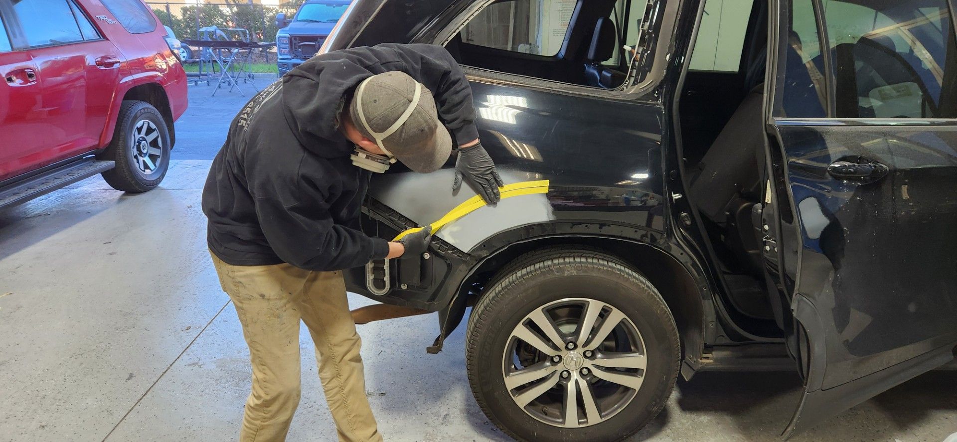 A person repairs a black SUV's rear quarter panel in a garage.