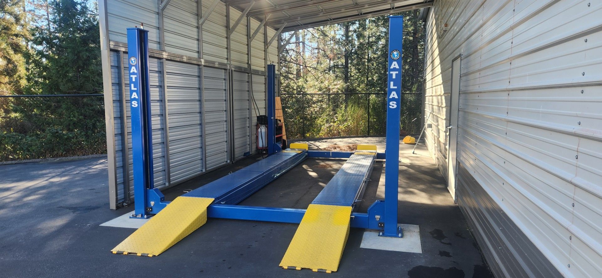 A blue and yellow car lift inside a metal structure. Trees are visible in the background. 