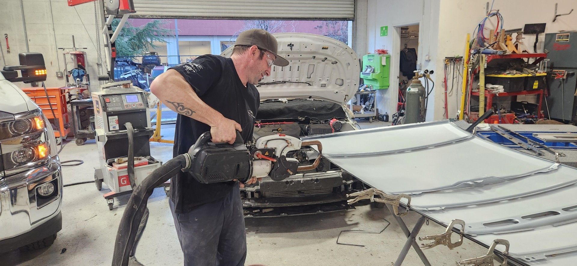 Man in auto repair shop uses a blower on car parts.