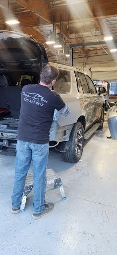 A person working on a vehicle in a repair shop. They are standing on a small stepladder.