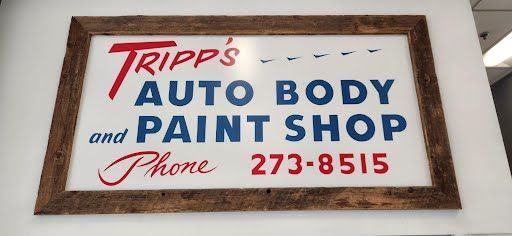 Sign for Tripp's Auto Body & Paint Shop, white background, framed in brown wood, red and blue text, phone number 273-8515.