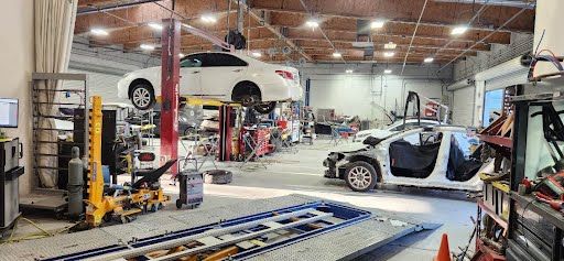 Auto body shop interior with two cars in repair. One elevated on a lift, one partially disassembled.