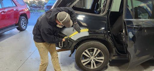 A person wearing a mask works on a black car in a repair shop.