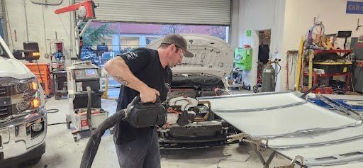 Man in auto repair shop uses a blower on car parts.
