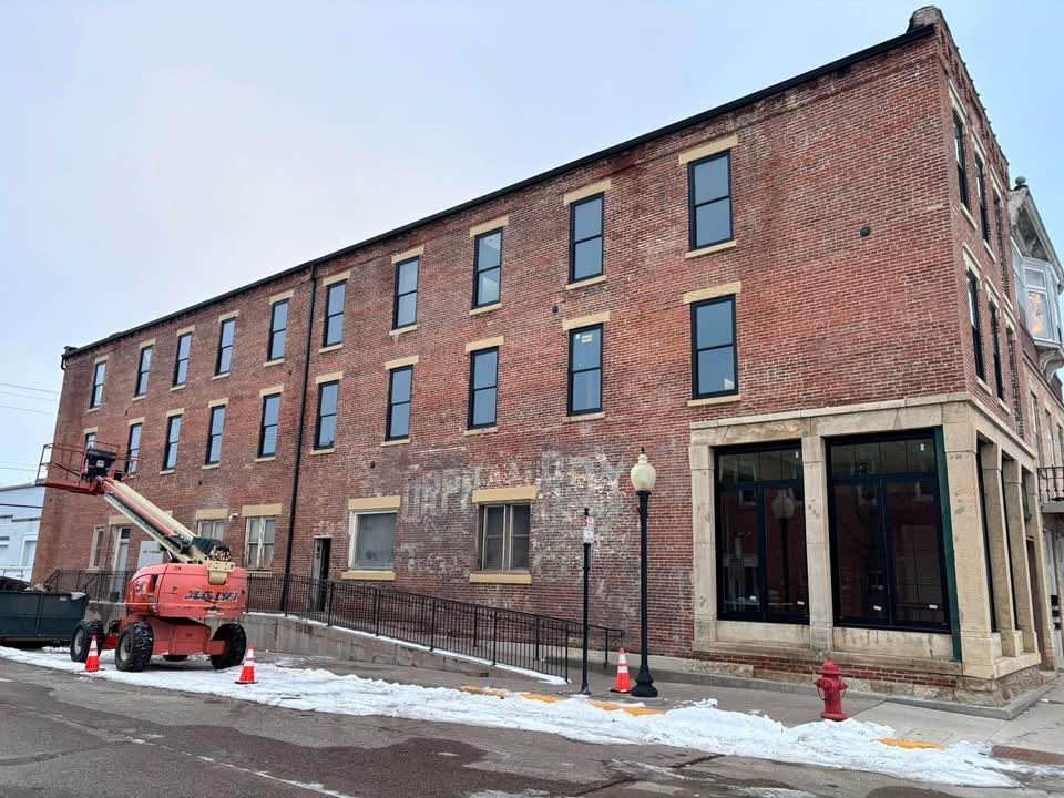 A red brick three-story building undergoing renovation, featuring a construction lift on the snowy street and a fire hydrant.