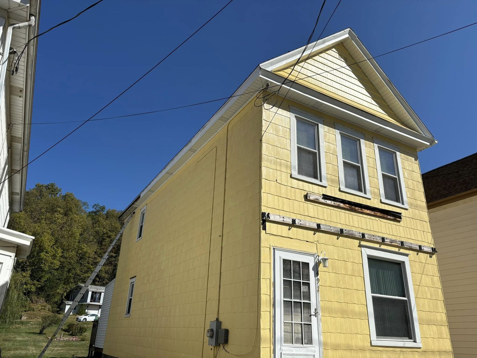 A two-story, yellow-sided house with a gabled roof against a bright blue sky.