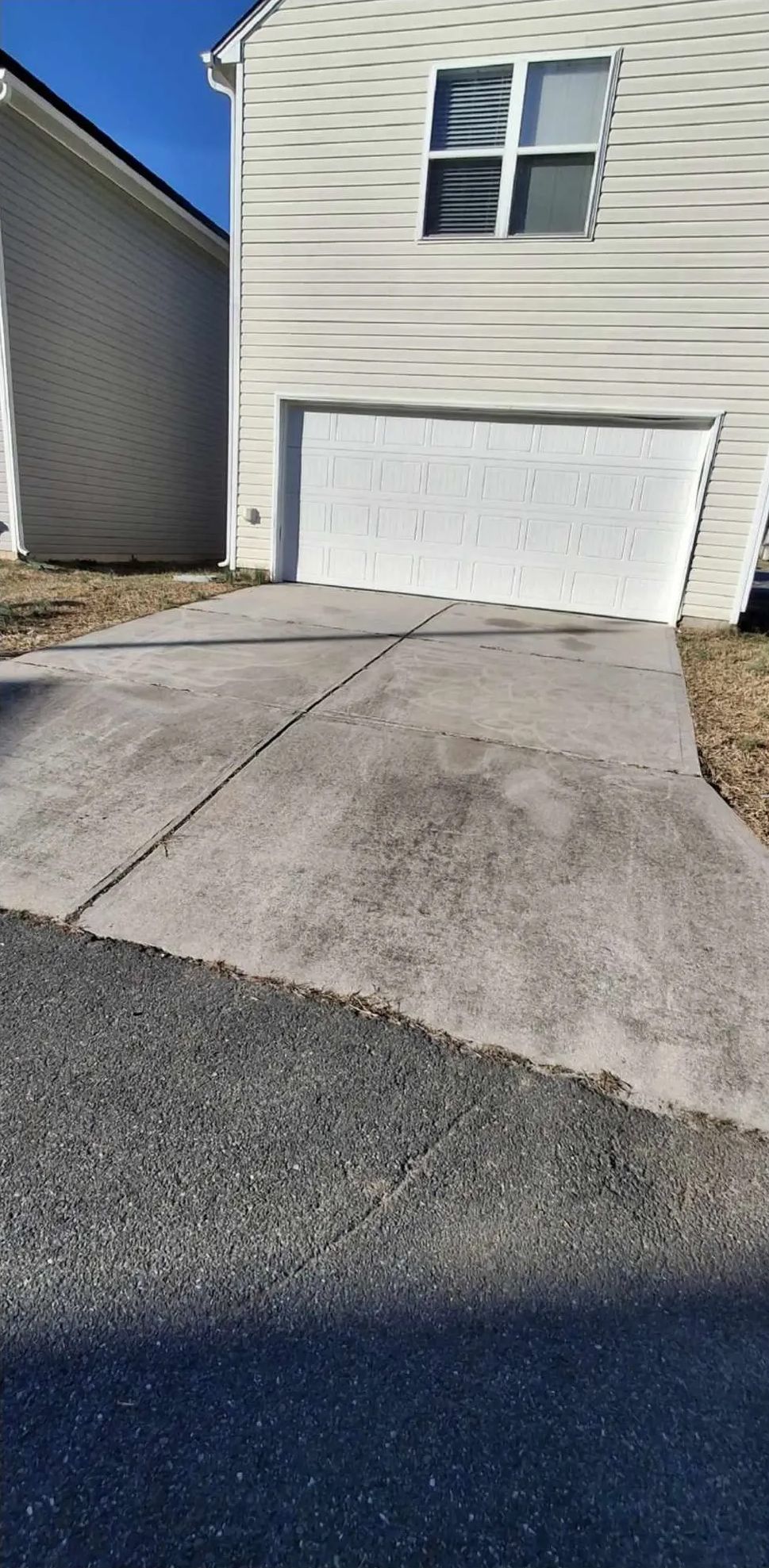 Concrete driveway leading to a white garage door, next to a beige house, under a blue sky.
