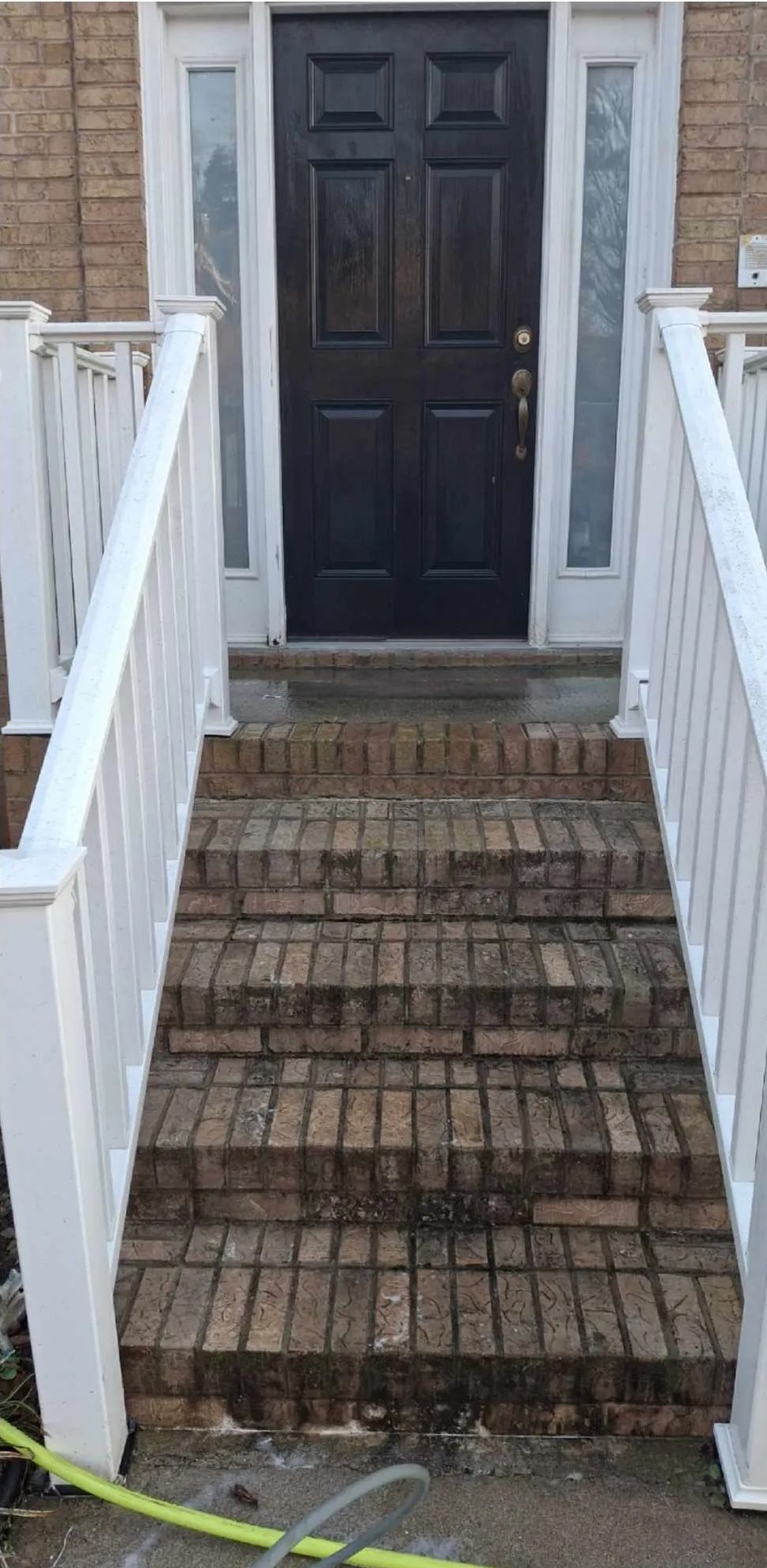 Exterior view of a brick staircase leading up to a dark front door, white railings on either side.