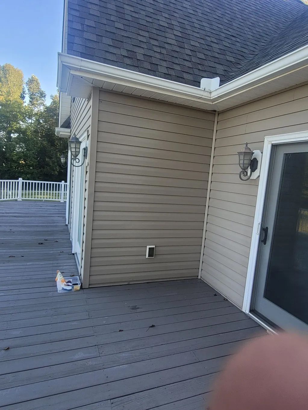 Tan sided house corner with deck and sliding door, outdoor lights, white trim.