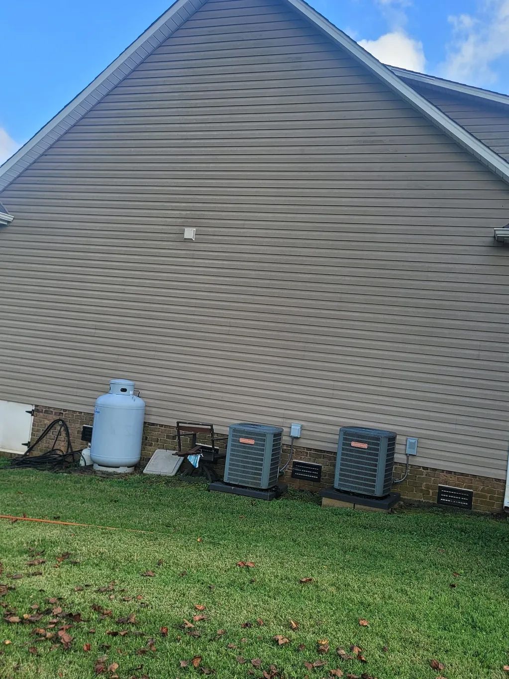Exterior house with propane tank and two air conditioning units on grassy lawn. Blue sky.
